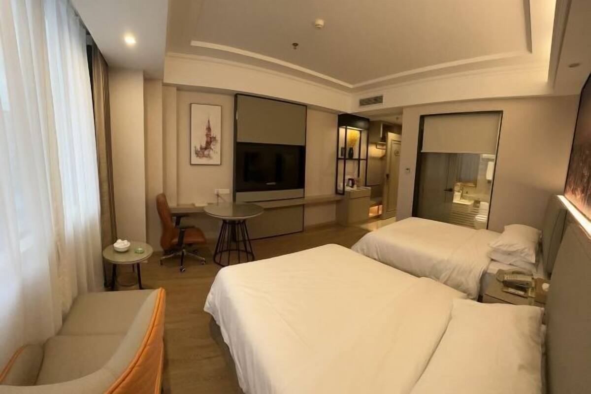 A hotel room with two beds, a desk, a chair, a TV, and a large mirror.
