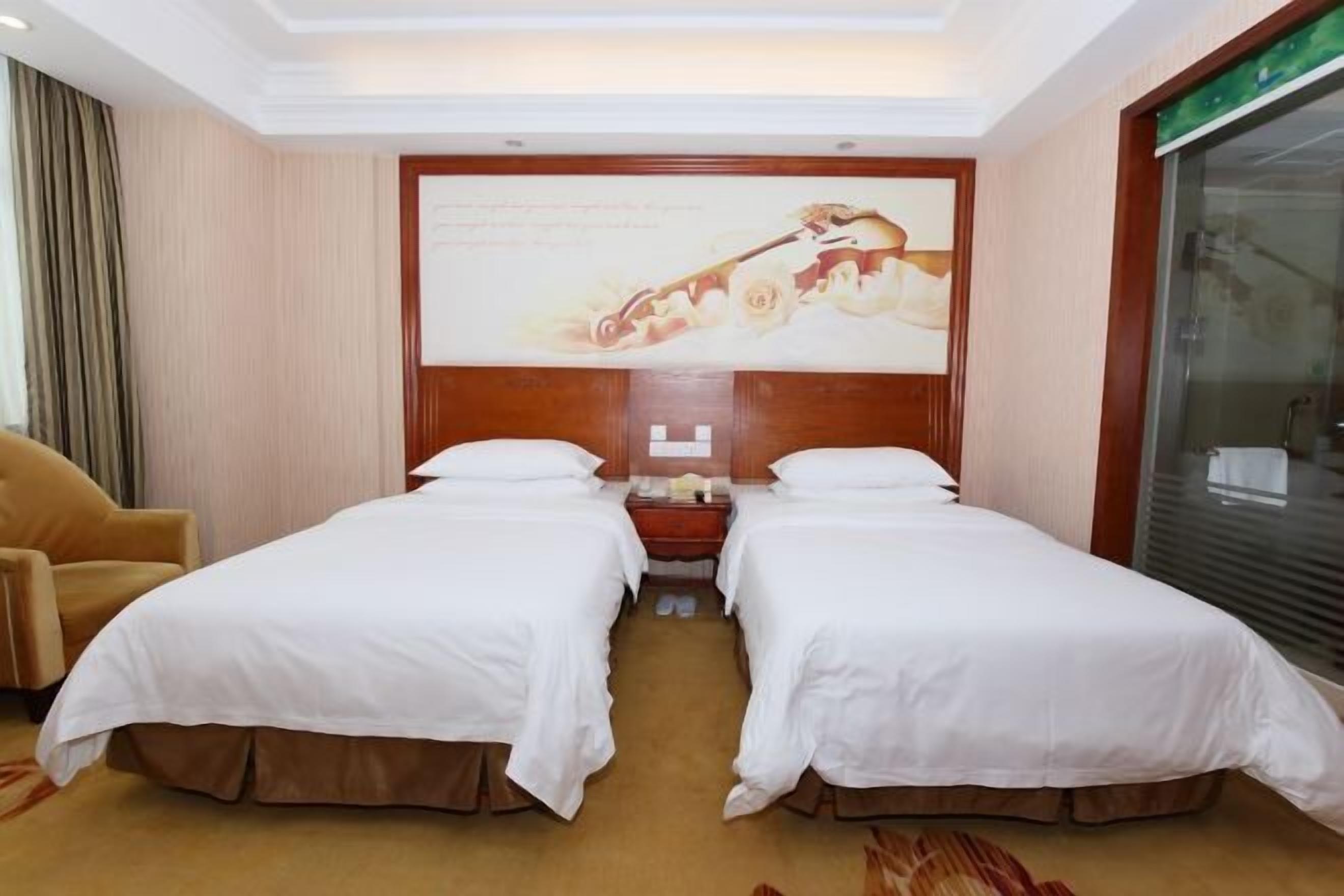 A hotel room with two single beds, a wooden headboard, a nightstand, a chair, and a large window.