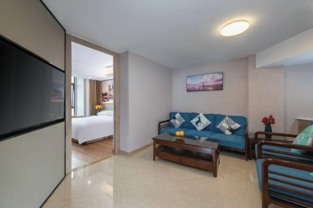 A modern hotel room with a large bed, a blue sofa, a coffee table, and a TV.