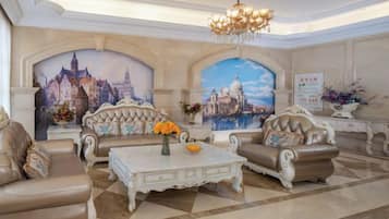 Un salon luxueux, agrémenté de canapés richement décorés, d’une table basse blanche et d’un lustre.