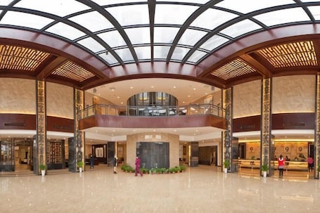 A spacious lobby with a high ceiling, a central fountain, and a reception desk.. Sanjianghe International Hotel