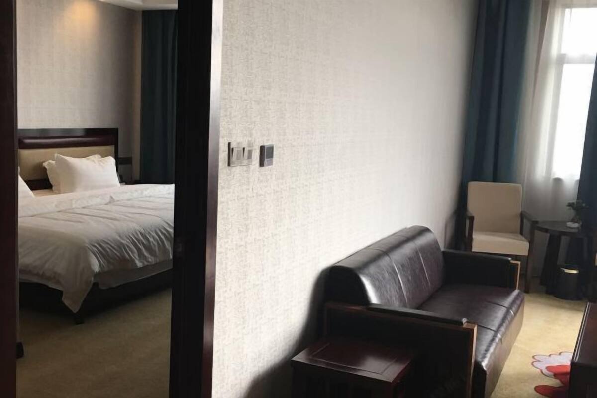 Hotellihuone, jossa on sänky, nahkasohva, pieni pöytä ja tuoli.