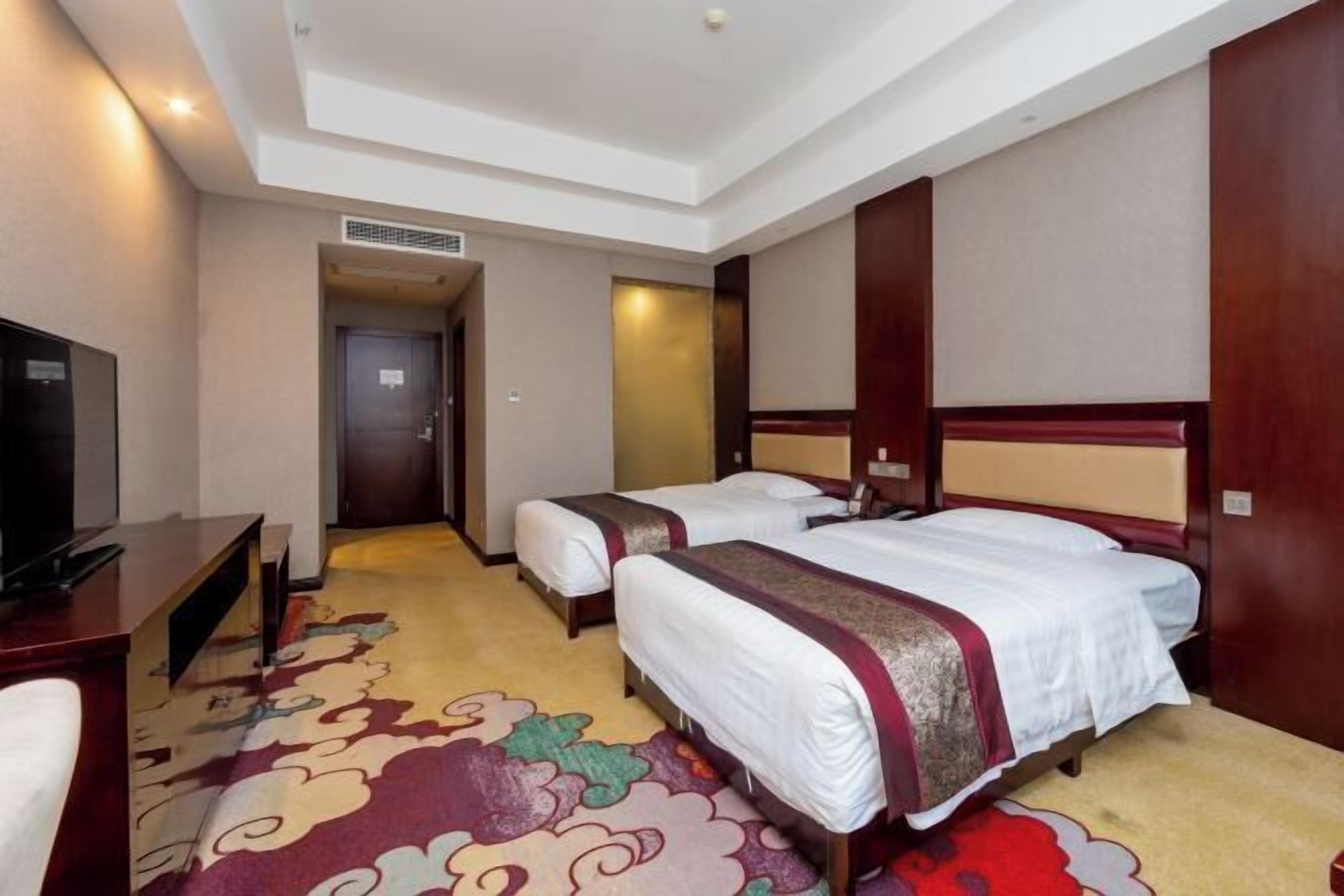 A hotel room with two beds, a desk, and a television.