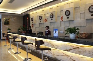 Zona de recepción de un hotel con mostrador de mármol, taburetes de bar y un recepcionista.