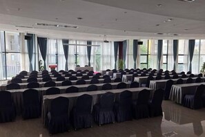 A conference room with rows of tables and chairs, large windows, and a stage. - Sanjianghe International Hotel (Pingle)