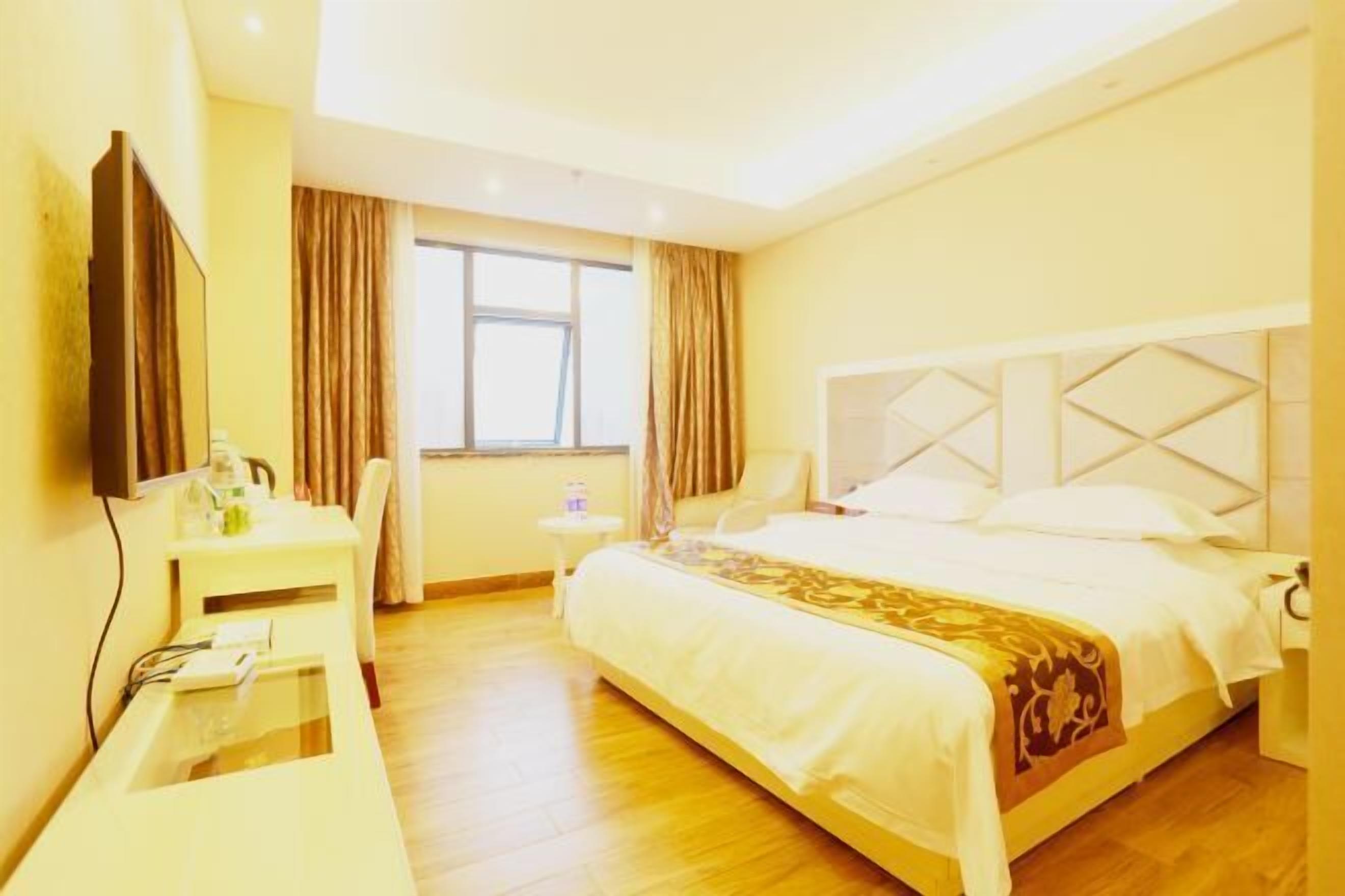 A hotel room with a bed, a desk, a chair, a TV, and a window with curtains.