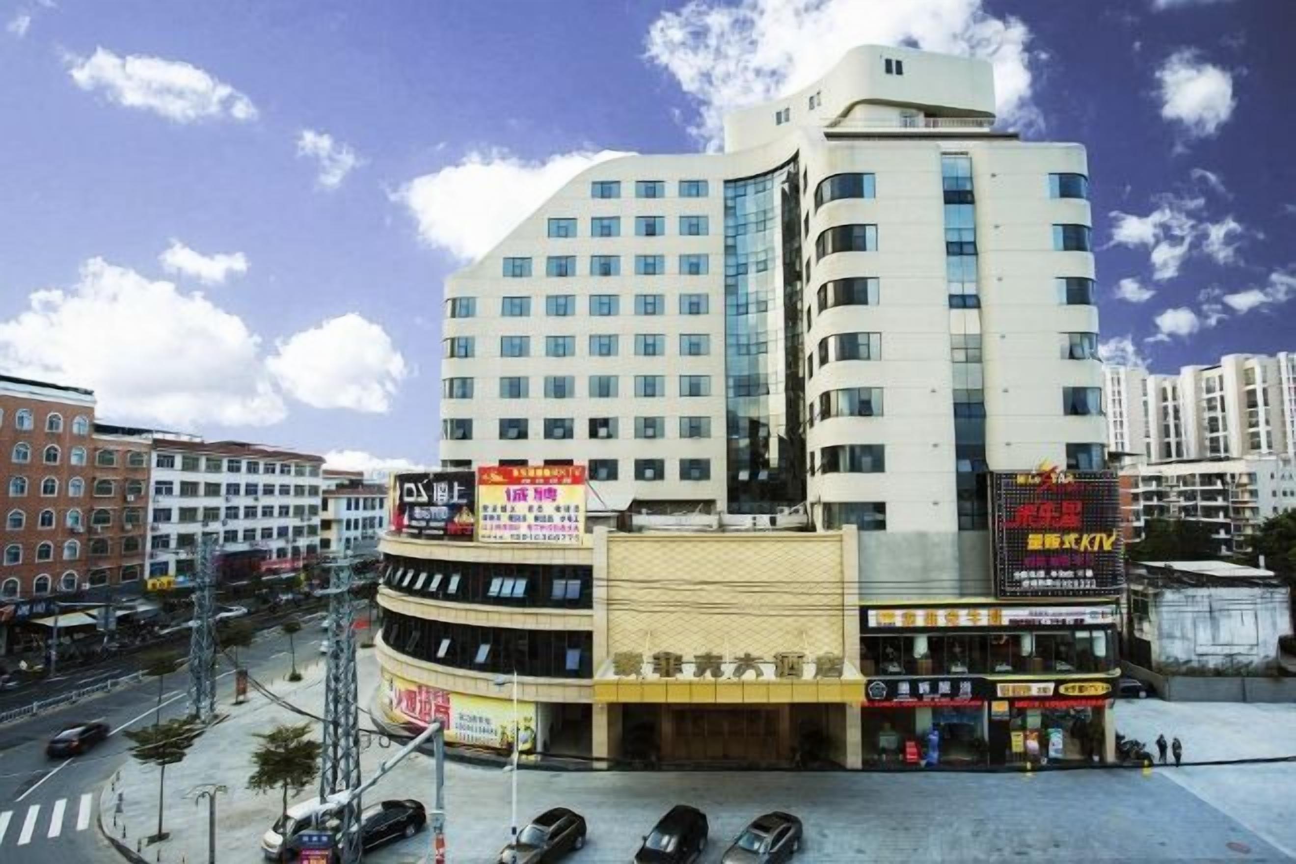 Un hotel de varios pisos con fachada curva, múltiples balcones y una zona comercial en la planta baja con señalización.