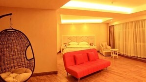 A hotel room with a hanging chair, a red sofa, a bed with a white headboard, a small table, and a window with curtains. - Suofeike Hotel (Pinghe)