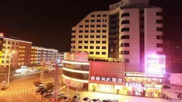 Un hotel de varios pisos en una ubicación destacada en la esquina, con una fachada muy iluminada y un estacionamiento con varios coches.
