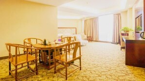 A hotel room with a dining area featuring a wooden table and chairs, a bed with a headboard, a desk with a chair, and a large window with curtains. - Suofeike Hotel (Pinghe)
