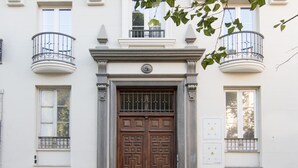 Facciata di un edificio con una porta in legno a due battenti, due balconi con ringhiere in metallo e una bicicletta parcheggiata davanti.