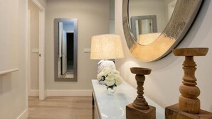 Un corridoio con uno specchio, una lampada e un tavolo in legno con un vaso di fiori.