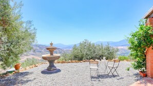 Un patio con una fuente de piedra, mobiliario exterior y vistas a montañas distantes.
