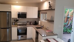 A modern kitchen with stainless steel appliances, a gas stove, and a built-in oven. There is a window with a view of a wooden deck and greenery. - Fully Furnished Studio, Private Parking, Laundry, Private Outdoor Space (Venice)