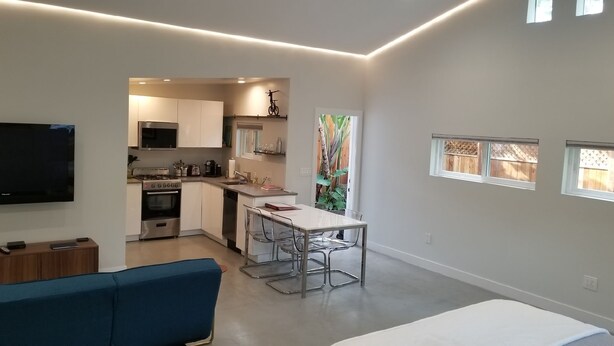 A modern kitchen with a dining area, a TV, and a blue sofa. - Fully Furnished Studio, Private Parking, Laundry, Private Outdoor Space (Venice)