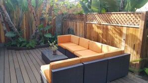 A wooden deck with a dark wicker sofa and a small table with a plant. - Fully Furnished Studio, Private Parking, Laundry, Private Outdoor Space (Venice)