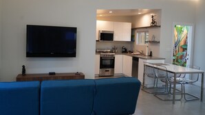 A modern living room with a flat-screen TV, a blue sofa, and a dining area with a glass table and chairs. - Fully Furnished Studio, Private Parking, Laundry, Private Outdoor Space (Venice)