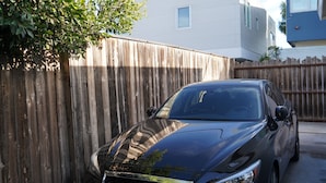 A black car parked in front of a wooden fence with a house in the background. - Fully Furnished Studio, Private Parking, Laundry, Private Outdoor Space (Venice)