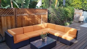 Una terraza de madera con un sofá modular y una mesa de centro de vidrio.