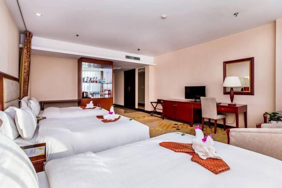 A hotel room with three beds, a desk, a television, and a minibar.