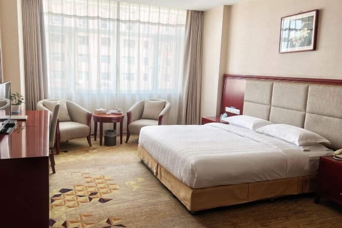 A hotel room with a bed, two chairs, a desk, a small table, and a window with curtains.