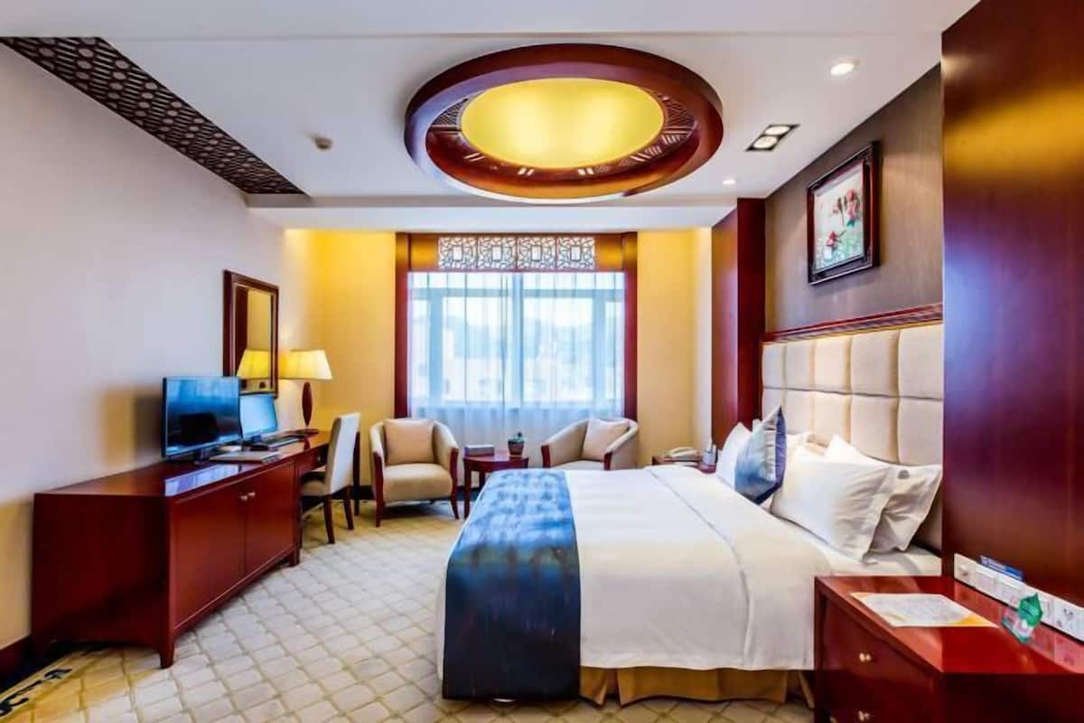 A hotel room with a bed, desk, chairs, a TV, and a window with curtains.