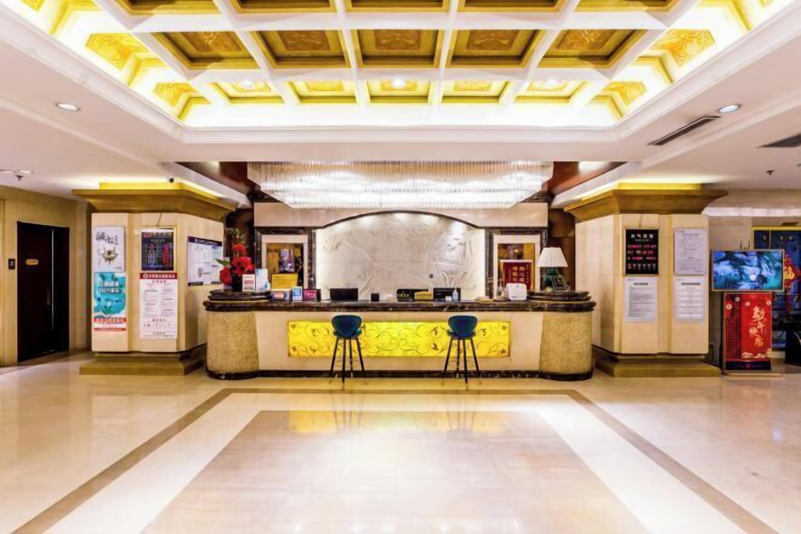 A hotel reception area with a central counter, two blue bar stools, and a decorative ceiling.