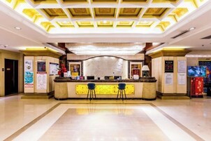Zona de recepción de un hotel con un mostrador central, dos taburetes azules y un techo decorativo.