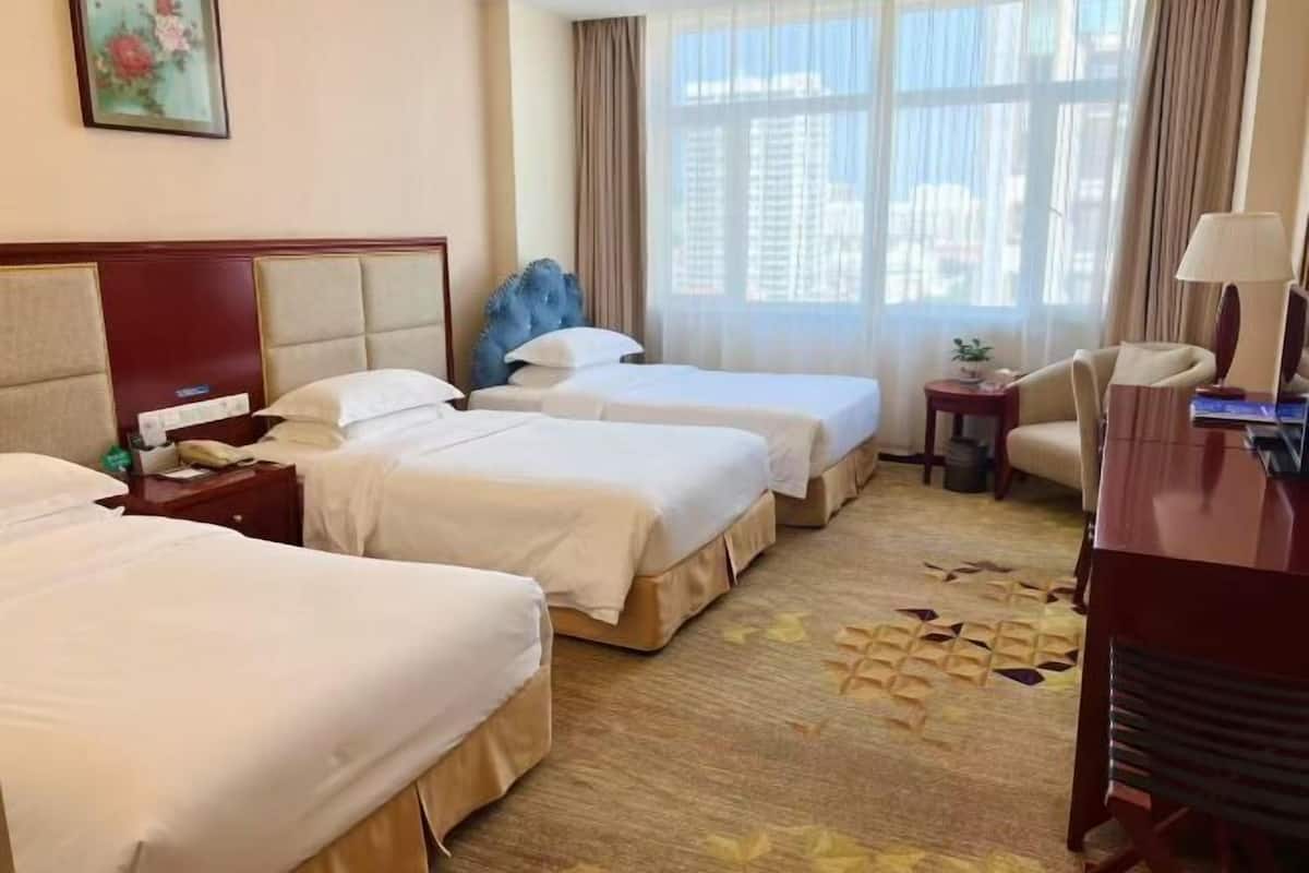 A hotel room with two beds, a desk, a chair, and a window with curtains.