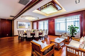 Una habitación amplia con comedor, una zona de estar con mesa de centro y ventanas grandes con cortinas.