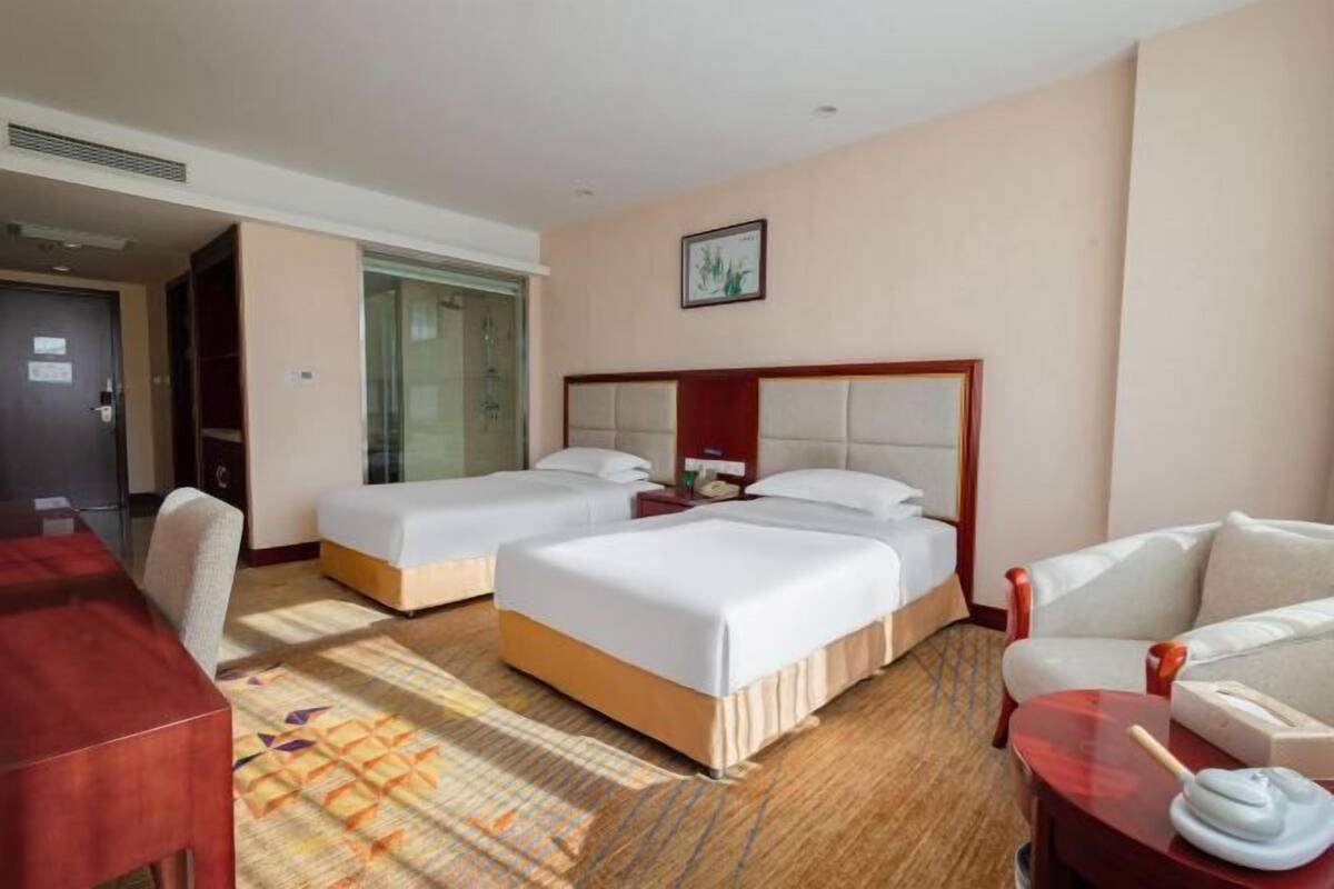 A hotel room with two beds, a desk, a chair, a sofa, and a patterned rug.