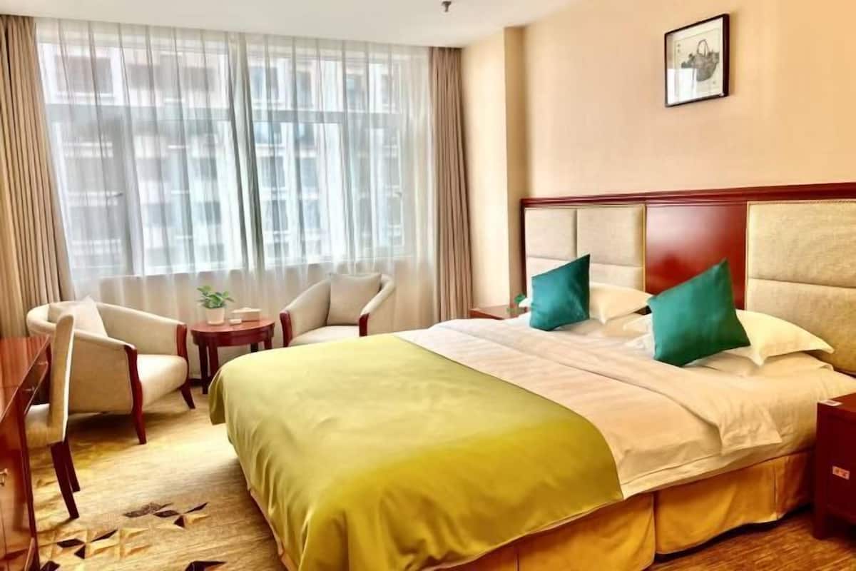 A hotel room with a bed, a desk, a chair, and a window with curtains.