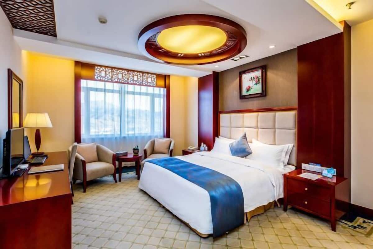 A hotel room with a large bed, a desk with a computer, a chair, a small table, and a window with a view.