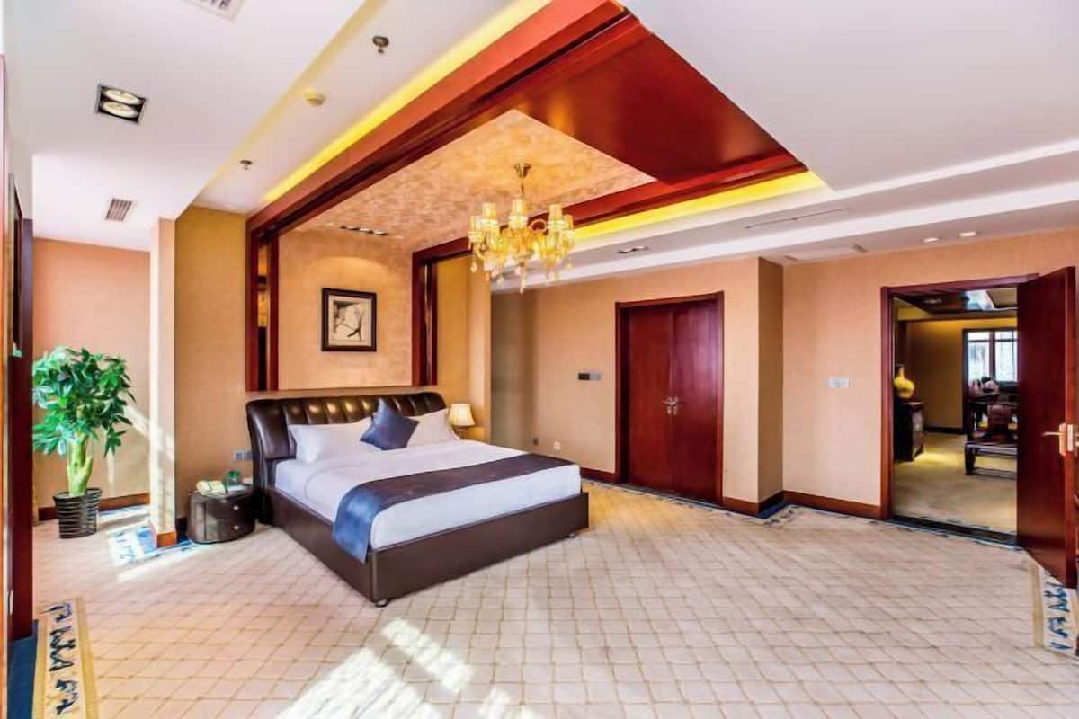 A spacious hotel room with a large bed, a chandelier, and a view of the hallway.