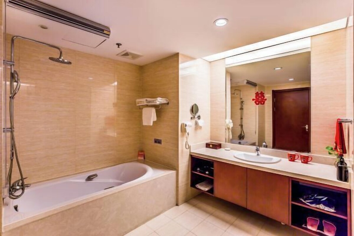 Un baño moderno con bañera, un espejo grande y tocador con lavamanos y toallero.