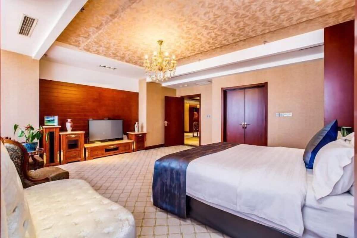 A hotel room with a large bed, a television, a wooden cabinet, and a chandelier.