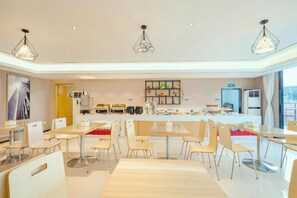 A modern dining area with multiple tables and chairs, a kitchen counter in the background, and pendant lighting. - City Comfort Inn Guilin Department Store (Guilin)