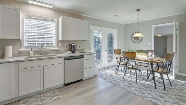 A modern kitchen with white cabinets, a built-in dishwasher, and a dining area with a wooden table and chairs. - Stay near all Chas attractions, quiet comfort with fenced yard! (Goose Creek)