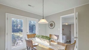 A dining area with a wooden table, chairs, a hanging light fixture, and a clock on the wall. - Stay near all Chas attractions, quiet comfort with fenced yard! (Goose Creek)