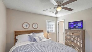 A bedroom with a bed, a ceiling fan, a TV on a wooden cabinet, and two wall-mounted picture frames. - Stay near all Chas attractions, quiet comfort with fenced yard! (Goose Creek)