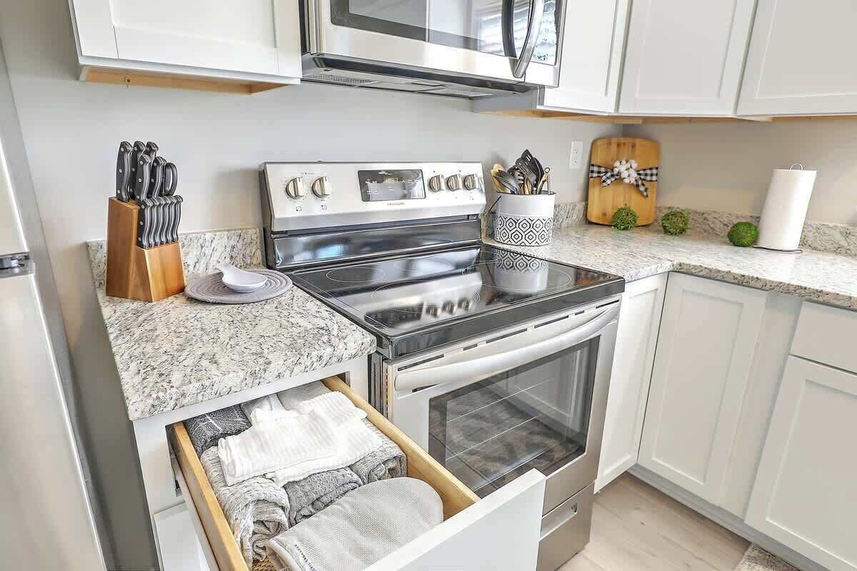 A kitchen with white cabinets, a stainless steel stove, and a microwave. There is a knife block, a cutting board, and a dish rack on the counter.