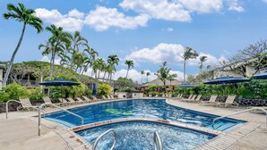 Una piscina con tumbonas y sombrillas, rodeada de palmeras y un cielo despejado.
