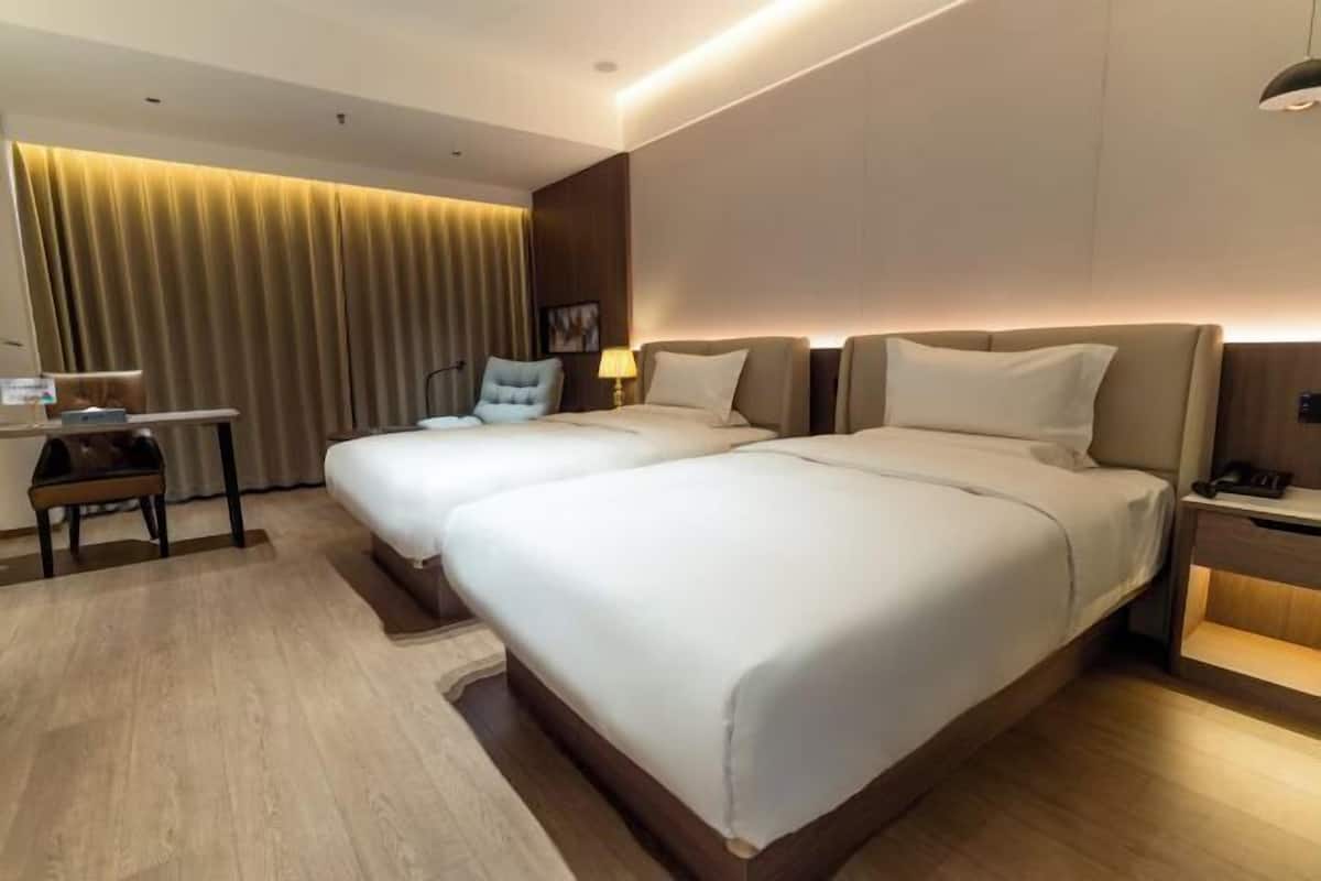 A hotel room with two beds, a desk, a chair, a lamp, and a curtain.