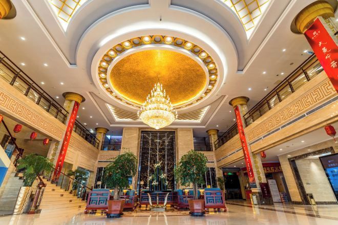 A spacious lobby with a grand chandelier, a central staircase, and red pillars.