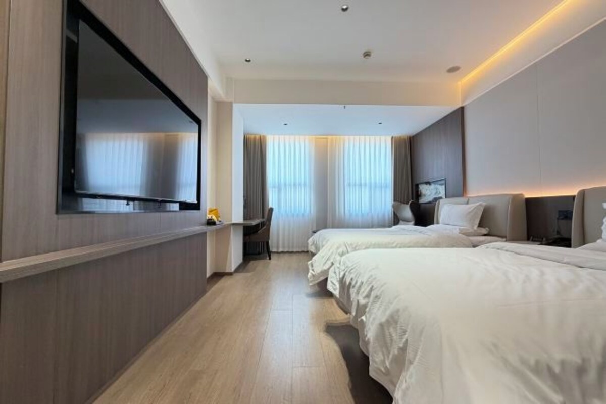 A hotel room with two beds, a large TV, a desk, and a chair.