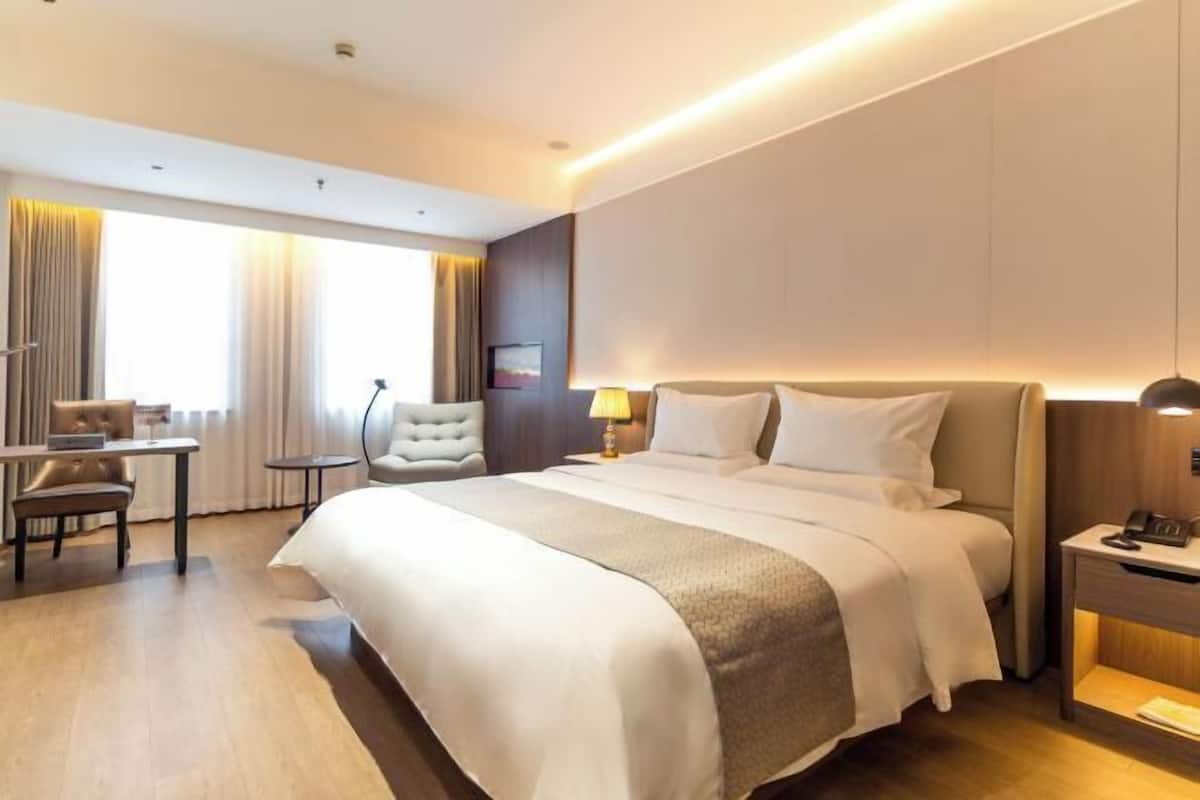 A hotel room with a large bed, a desk, a chair, and a small table.