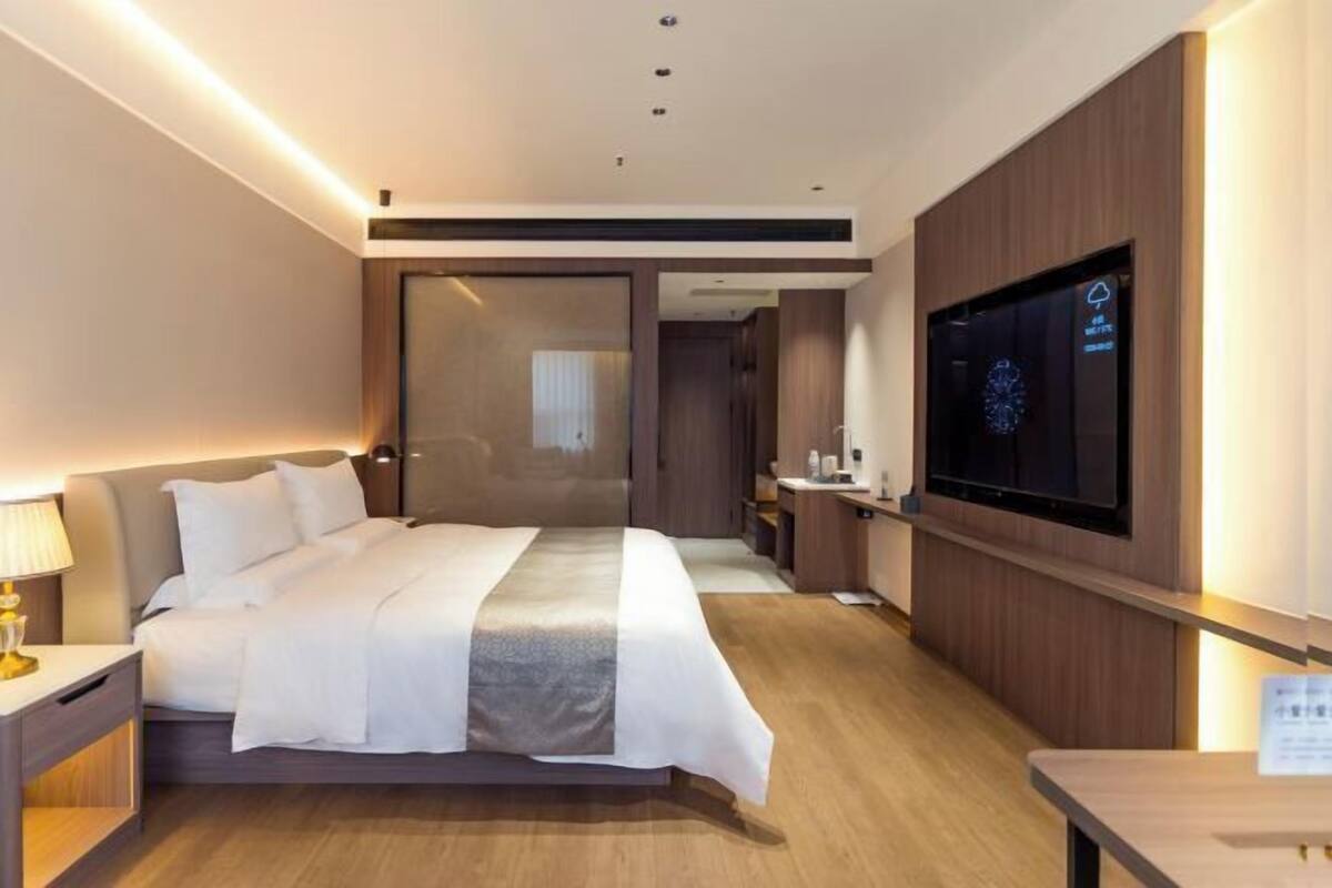 A modern hotel room with a bed, bedside table, TV, and a wooden floor.