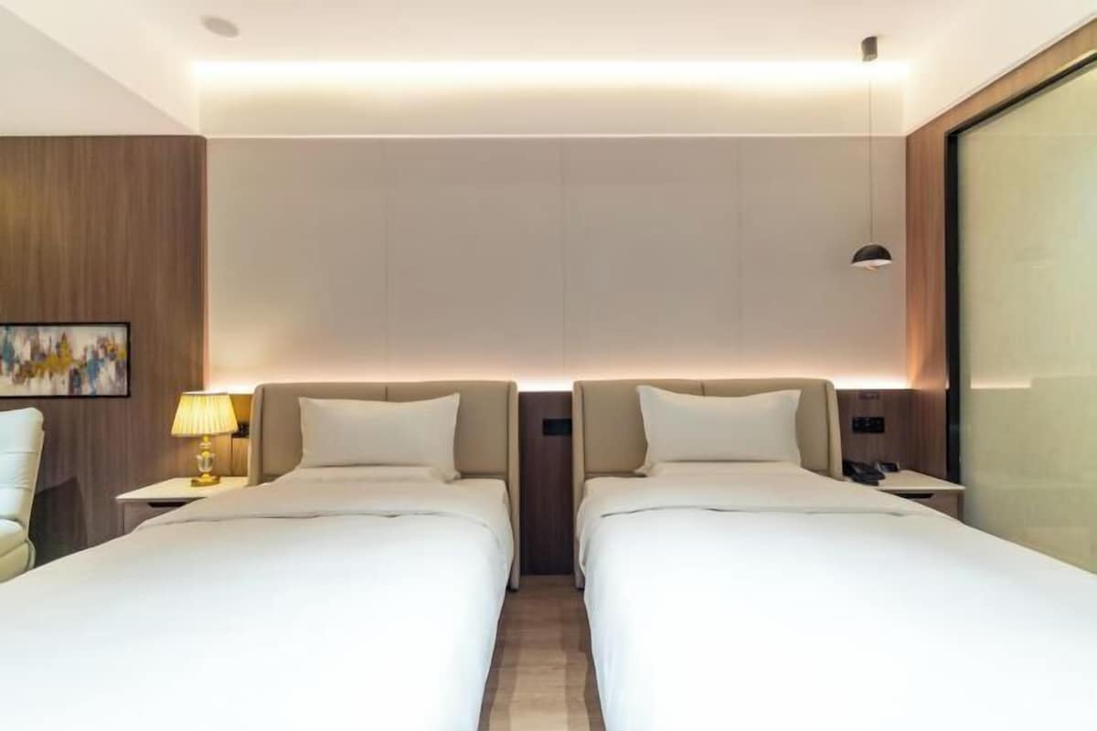 Una habitación de hotel con dos camas, una mesita de noche con lámpara y un ventanal grande.