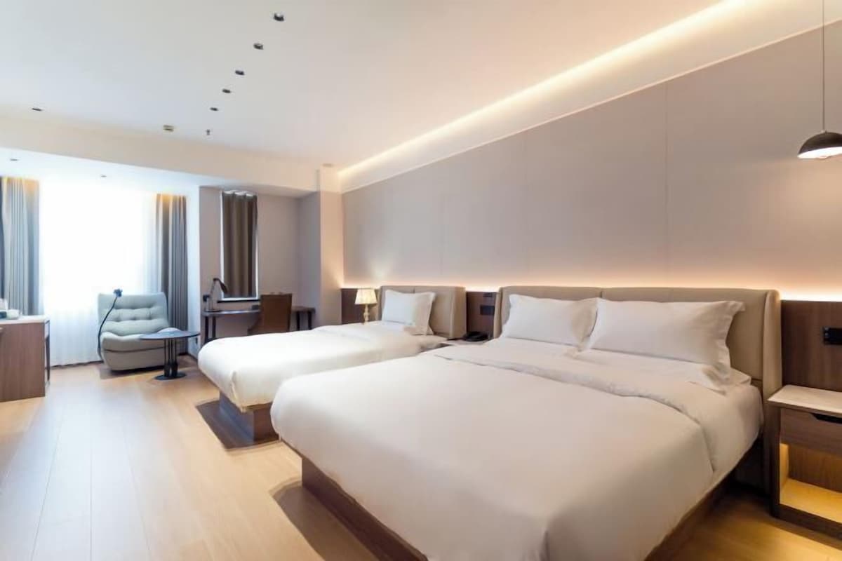Una habitación de hotel con dos camas, una silla, un escritorio y una lámpara.