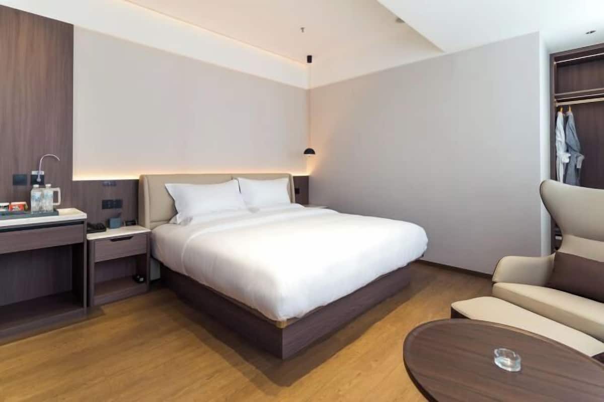 A modern hotel room with a large bed, a desk with a lamp, a chair, and a small table.